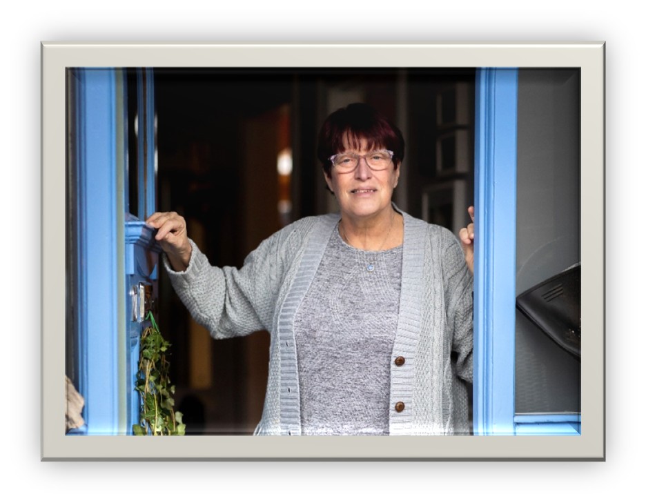 A women with glasses opening a blue door to welcome someone inside the building